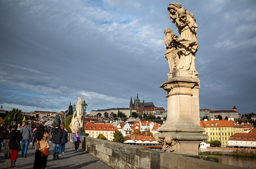 A photo of tourists crossing the Charles Bridge in Prague, Czech Republic.  The Charles Bridge is a medieval stone arch bridge that crosses the Vltava River in Prague and was constructed in 1357.