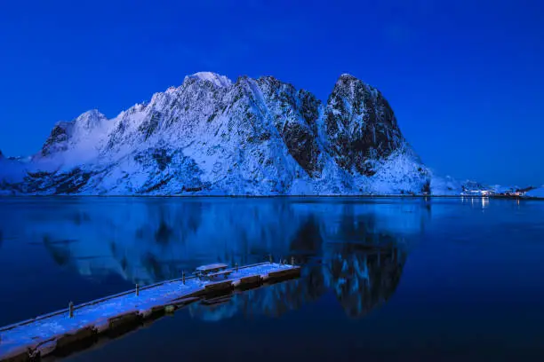 Photo of Olstind mountain peak above the fjord in blue hour with a tint of sunset, a wooden pier