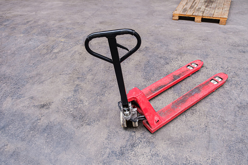 Old hand pallet truck. Worn pallet jack on the concrete floor of a large warehouse.