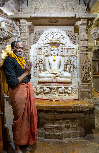 Jaisalmer, India - February 12, 2024: praying man in front of a buddha statue Chandraprabha or Lord of Moon at the Jain temple in Jaisalmer, India.