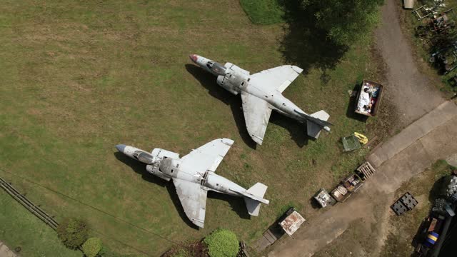Aerial Birdseye view circling two military Sea Harrier jets on grassy Charlwood logistics yard, Surrey