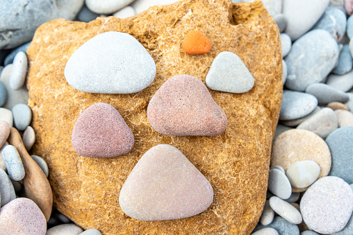 Triangular pebbles in varying colors artistically placed on a large, textured yellow rock, set against a pebble background