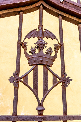 Valencia, Valencia - Spain - 09-08-2021: Close-up of a rusted crown design on an iron gate against a yellow wall