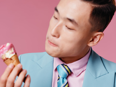 Asian man with ice cream in his hands on a pink background. High quality photo