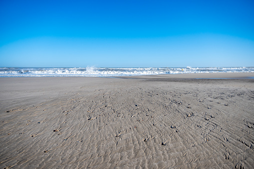 Pristine sandy beach with rippled textures leading to lively waves under a clear blue sky