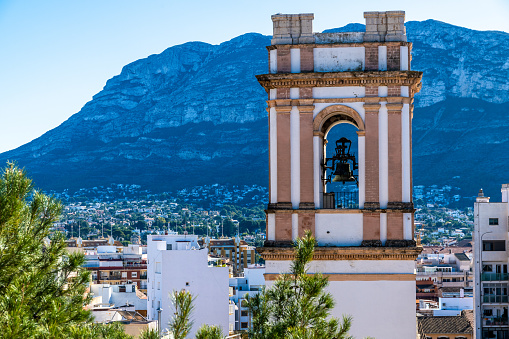 Denia, Alicante - Spain - 12-22-2023: Bell tower stands over Denia, Spain, with the majestic Montgo Mountain rising in the background