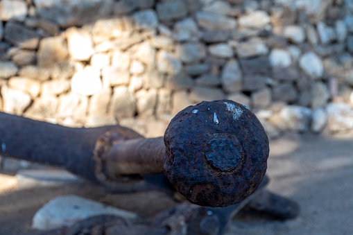 Denia, Alicante - Spain - 12-22-2023: Detailed close-up of a corroded iron anchor against a blurred stone background