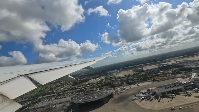 Wing view from a commercial jetliner taking off from a bustling airport during daytime