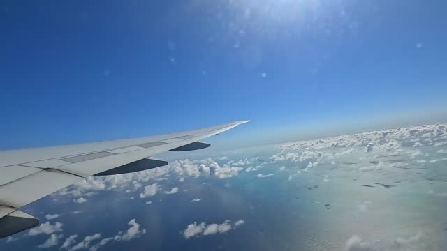 Serene view of airplane wing soaring above fluffy clouds in a clear blue sky