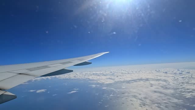 Serene view of airplane wing soaring above fluffy clouds in a clear blue sky