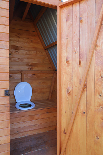 Open door of rural wooden toilet, empty inside, in vertical format