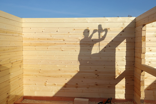 Shadow on wooden wall from builder working on top of house under construction, with copy space