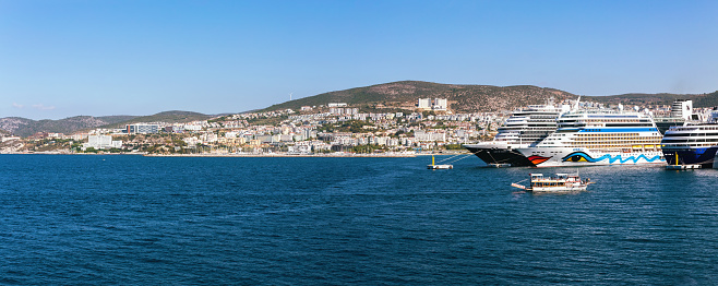 Kusadasi panorama and big sea cruise liners moored in the port. Blue sky at background. Light blue and turquoise seasurface. Bright summer day. October 18, 2023. Kushadasi, Turkey Turkiye)
