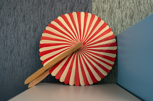 A round vintage red and cream striped fan unfolded on a table in a corner.