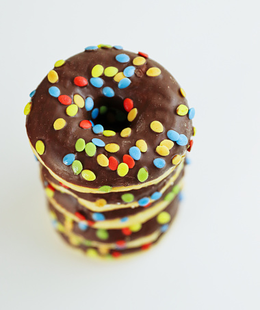 A stack of doughnuts glazed with chocolate and colorful smarties. Pile of 5 donuts isolated on a white background. Side view. Copy space