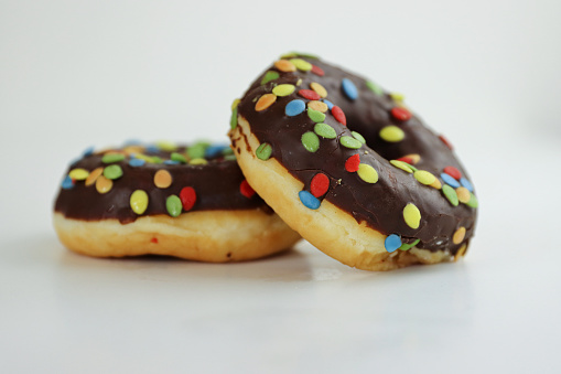 A stack of doughnuts glazed with chocolate and colorful smarties. Pile of 2 donuts isolated on a white background. Side view. Copy space