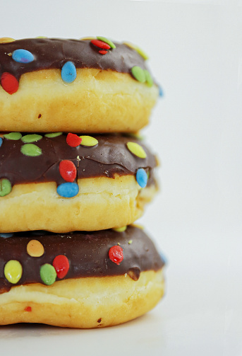 A stack of doughnuts glazed with chocolate and colorful smarties. Pile of 3 donuts isolated on a white background. Side view. Copy space