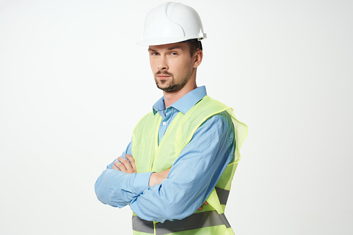 An architect or civil engineer stands with rolled up planning documents and a safety vest in front of a foundation under construction on the construction site and wears a white hard hat. Photographed in high resolution with copy space