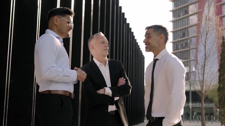 Meeting of three diverse business men outdoor chatting carefree on break. Formal professional people