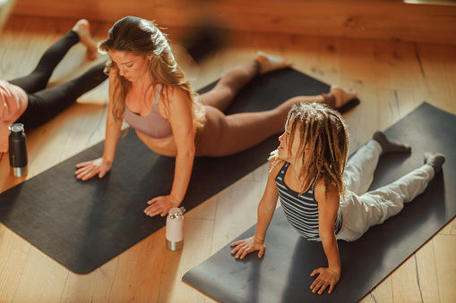 Children join their mother in a yoga session at home, practicing poses on mats with focus and enjoyment, highlighting the importance of health and family bonding through exercise.