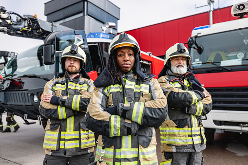 Male and female firefighters wearing fire protective gear, looking at the camera while standing in front of the fire engine.