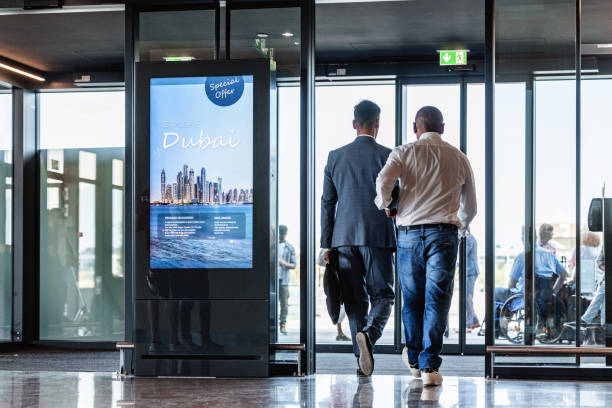Latin American Driver Picking Up A Client At The Airport Full length shot from behind with blurred background of two men walking and about to cross the exit door of the airport, the one on the right is a Latin-American driver who arrived to pick the other one up. walking into glass door stock pictures, royalty-free photos & images