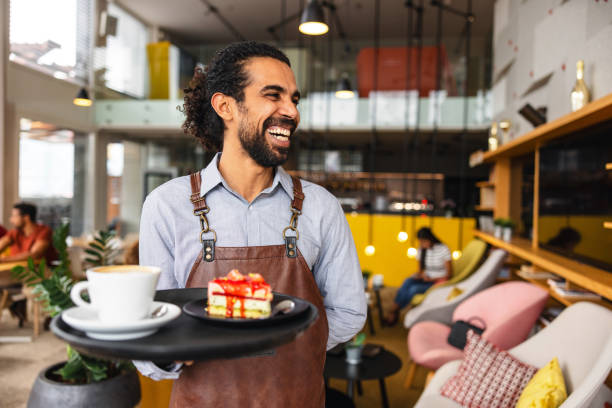 Happy Male Middle Eastern Bartender Laughing While Carrying A Tray With Drinks At A Bar