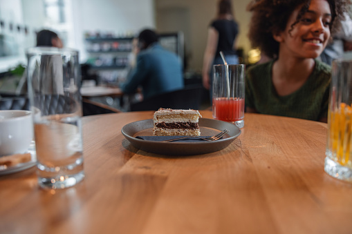 A slice of delicious and sweet cake served to a young black girl at a coffee shop. The focus is on the cake while the background is slightly blurred. In the back the young girl is visible.