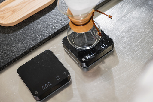 Two small scales placed on a steel countertop ready to be used for preparation of pour-over coffee at a cafeteria.