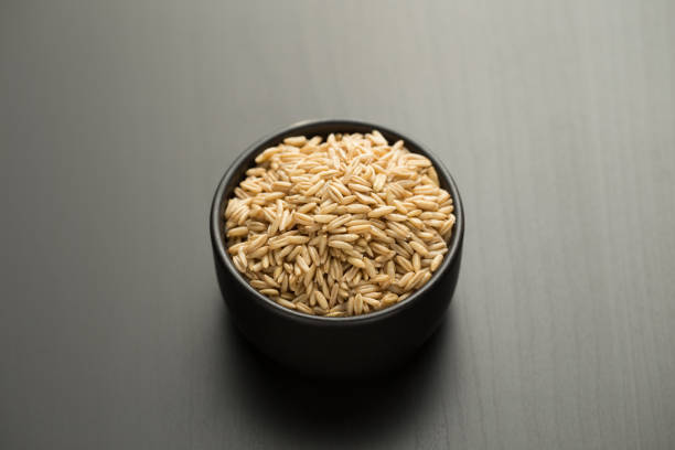 Oats rice in a small black bowl on a black wooden table.
