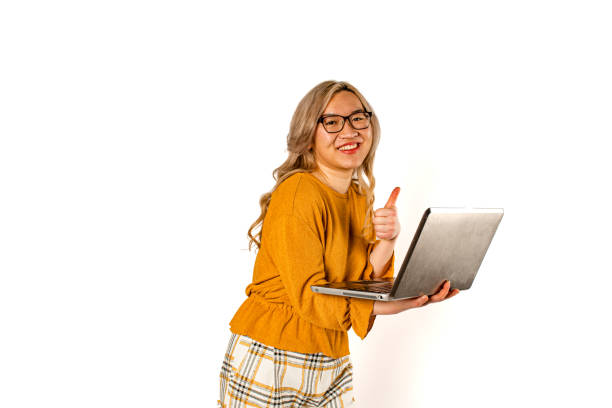 With a beaming smile, an Asian woman immerses herself in her laptop, embodying the excitement and potential of modern technology in our studio shot