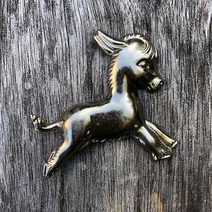 A silver-colored pressed metal lapel pin of a baby burro or donkey from the early 1950s rests on gray weathered wood.