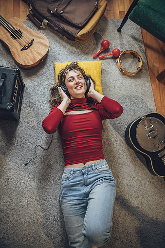 Charming young woman listening music on headphones while lying on the floor in living room.