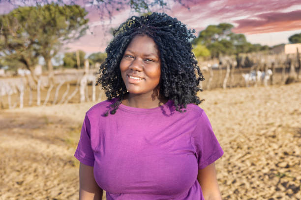 african woman , in the village, standing in the yard sandy area in front of the pen with livestock