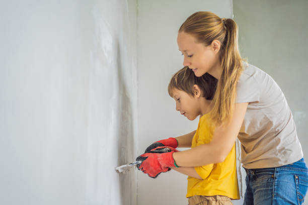 woman with hir son makes repairs at home, she teaches boy to plaster the walls with a spatula in his hands - plaster plasterer work tool child imagens e fotografias de stock