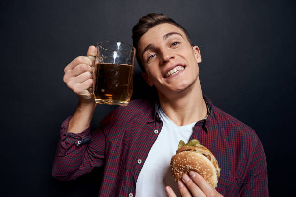 istock man with beer mug and hamburger in hands fun lifestyle studio dark isolated background 2051888974