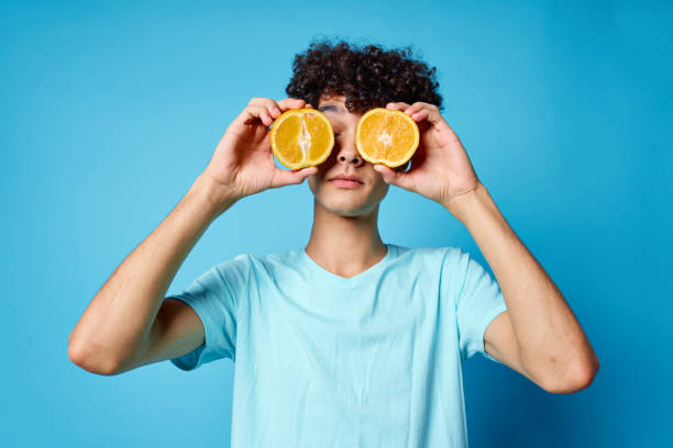 istock guy with curly hair holding an orange fruit blue background 2051906317
