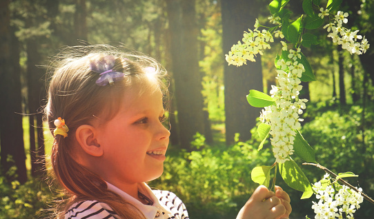 Little girl smelling blooming tree.  Happy child enjoying nature outdoors. Smiling child in the garden. Fairy nature