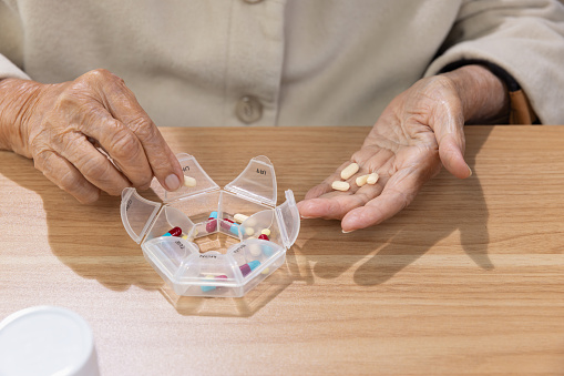 Elderly woman putting pills into pill box for the week.