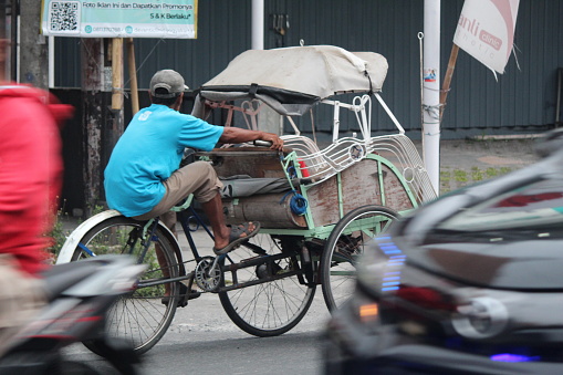 Yogyakarta, Indonesia, 10 December 2023; A pedicab driver pedaling a rickshaw on a sunny morning