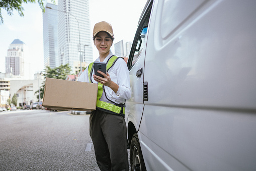 Portrait of an Asian courier woman with a smart phone delivering a package in the city.