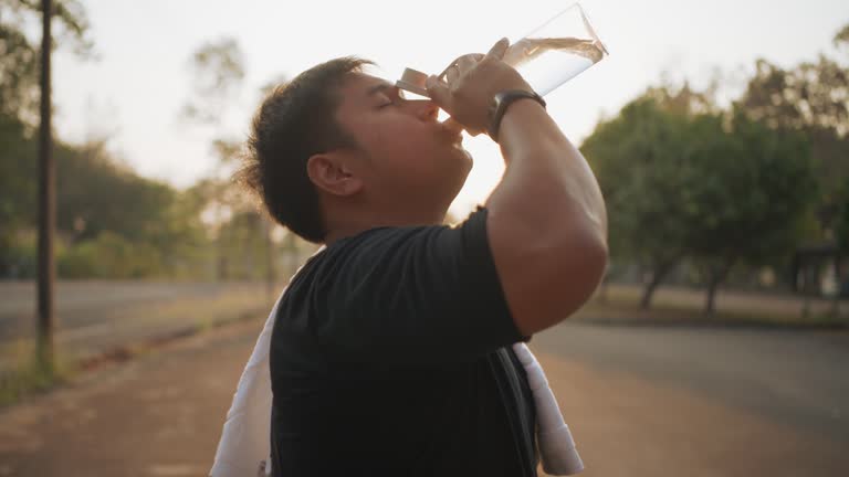 A male runner stops to drink water before his morning run at a local park, with sun flares