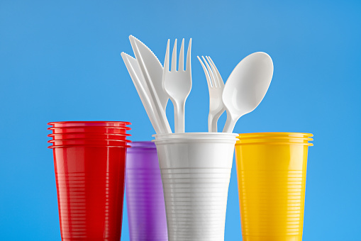 Set of multi-colored plastic cups with cutlery. Close up on blue.