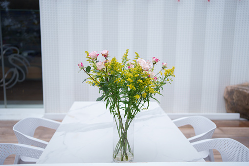 Bouquet of sunflowers in an aluminum can or retro vase, on a background of white curtains. On the table is a flower and fallen petals. View from the window. Rural or rustic background, selective focus, close-up.