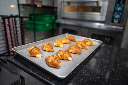 Croissants baking in the oven alongside a baking sheet filled with buns in a commercial kitchen at a cooking school