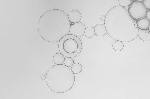 Abstract of art image of oil and water bubbles to create interesting pattern and shapes on gradient grey-silver background. Ideal as wallpaper, brochure, banner etc.,