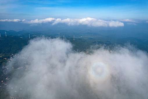 The wind turbine in the circular rainbow amidst the clouds and mist on the mountaintop