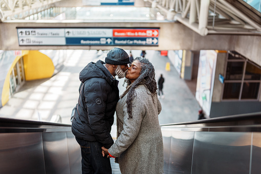 An active and adventurous senior couple of African American descent lean in for a kiss while riding down an escalator located in a train station in Washington DC.