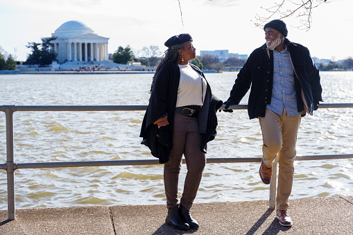 An active and loving senior couple of African American descent cheerfully talk while on a relaxing walk along a paved path in Washington DC, with a view of the Jefferson Memorial in the background.