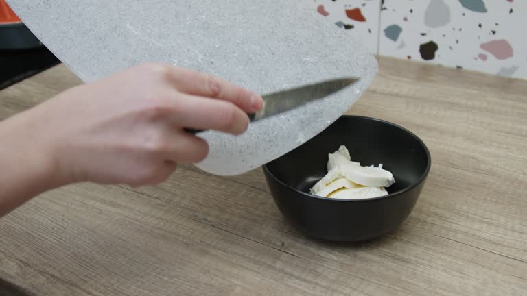 Female hands moving mozzarella slices into a bowl.